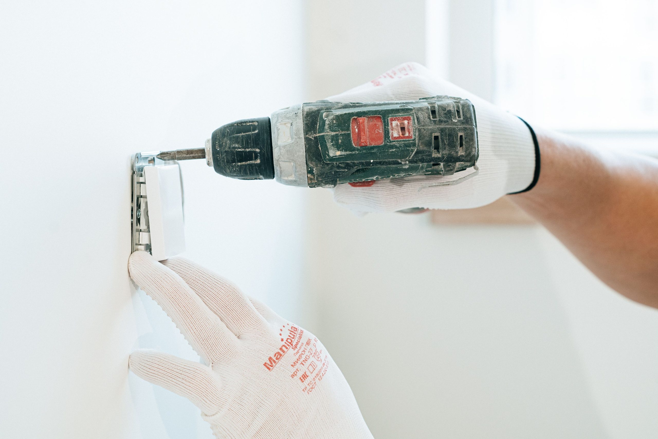 Mains gantées installant prise murale avec perceuse